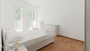 A bedroom with a bed, bedside table, nightstand, and a window with a view of trees. - GuestHost - Cozy 55 sqm apartment, perfect for 3 people, located on the second floor of a building with an elevator (NOT accessible to disabled guests).The property is located in the Corvetto neighborhood, in a quiet residential area just steps from Vett (Milan)