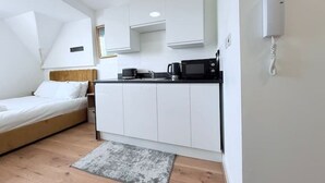 A compact bedroom with a bed, a kitchenette with a microwave, and a phone on the wall.