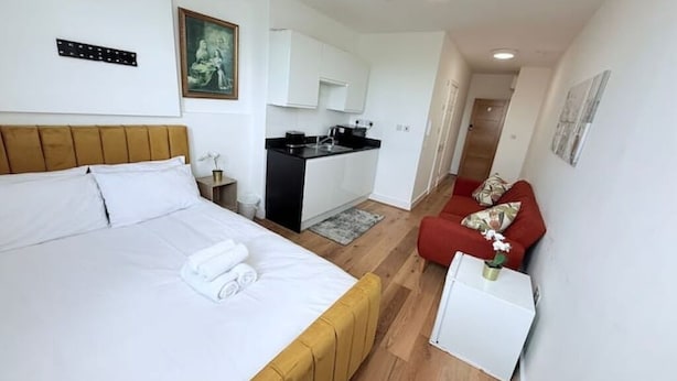 A bedroom with a bed, a small kitchenette, a red sofa, and a white cabinet.