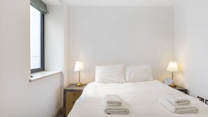 Hotellihuone, jossa on suuri sänky, kaksi yöpöytää valaisimineen, ikkuna ja peili seinällä.