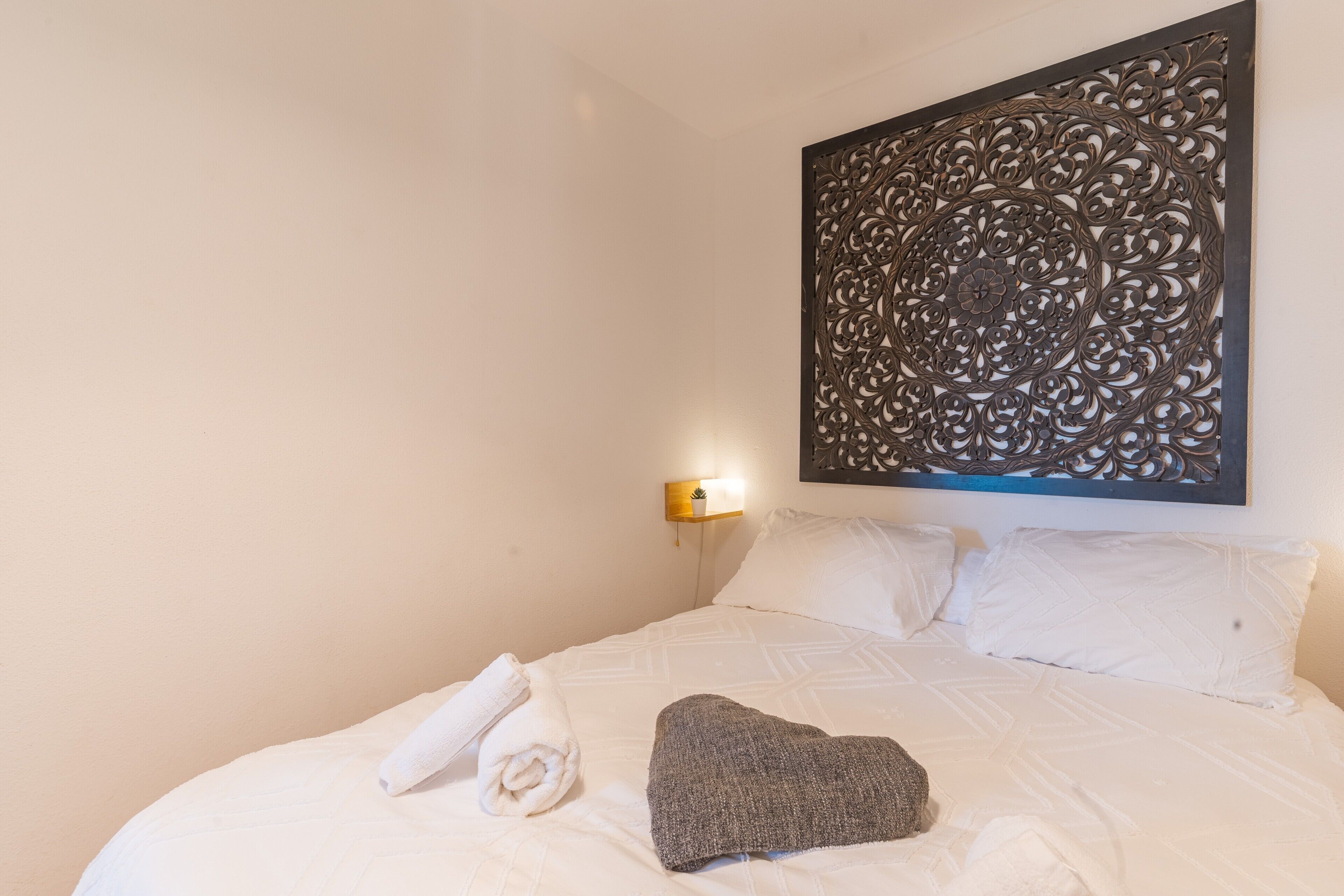 A neatly made bed with white linens, a rolled towel, and a gray throw blanket.