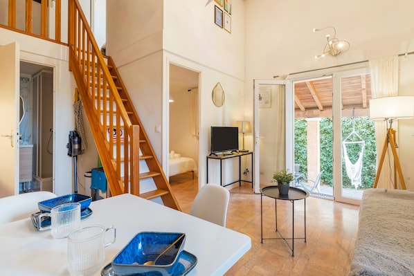 A spacious living area with a wooden staircase, a television, and a balcony with a view.