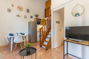A compact living space with a dining area, kitchen, staircase, and a TV on a stand.