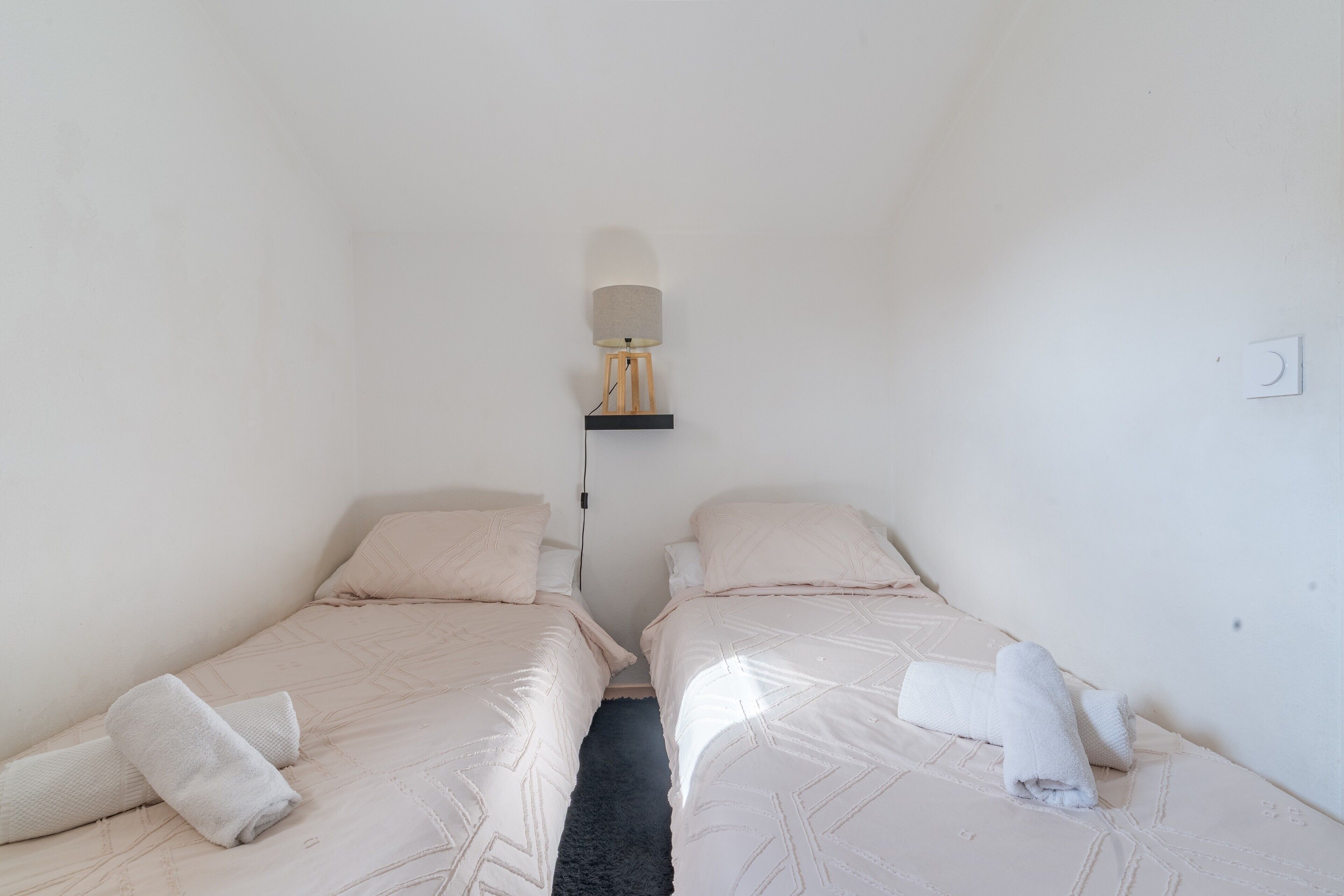 A small, clean room with two beds, a wall-mounted lamp, and a power outlet.