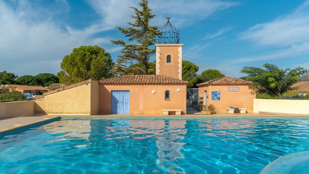 Uma área de piscina com um edifício que possui uma torre, uma porta e um banco.