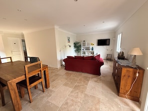 A living room with a red sofa, a wooden dining table, and a TV mounted on the wall. - Lower villa with garden - walking distance to town center and beach - ideal for families (Sainte-Maxime)