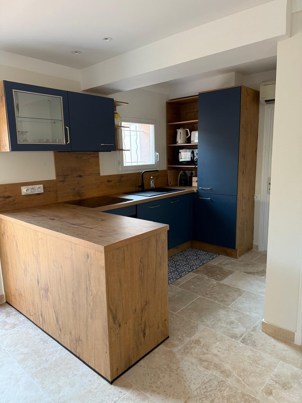A modern kitchen with a wooden island, dark blue cabinets, and a window providing natural light.