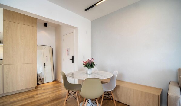 A modern kitchen with wooden cabinets, a marble countertop, and a dining area with a round table and chairs. - Evas - Charming Apartments With Sea View in Floripa (Florianópolis)