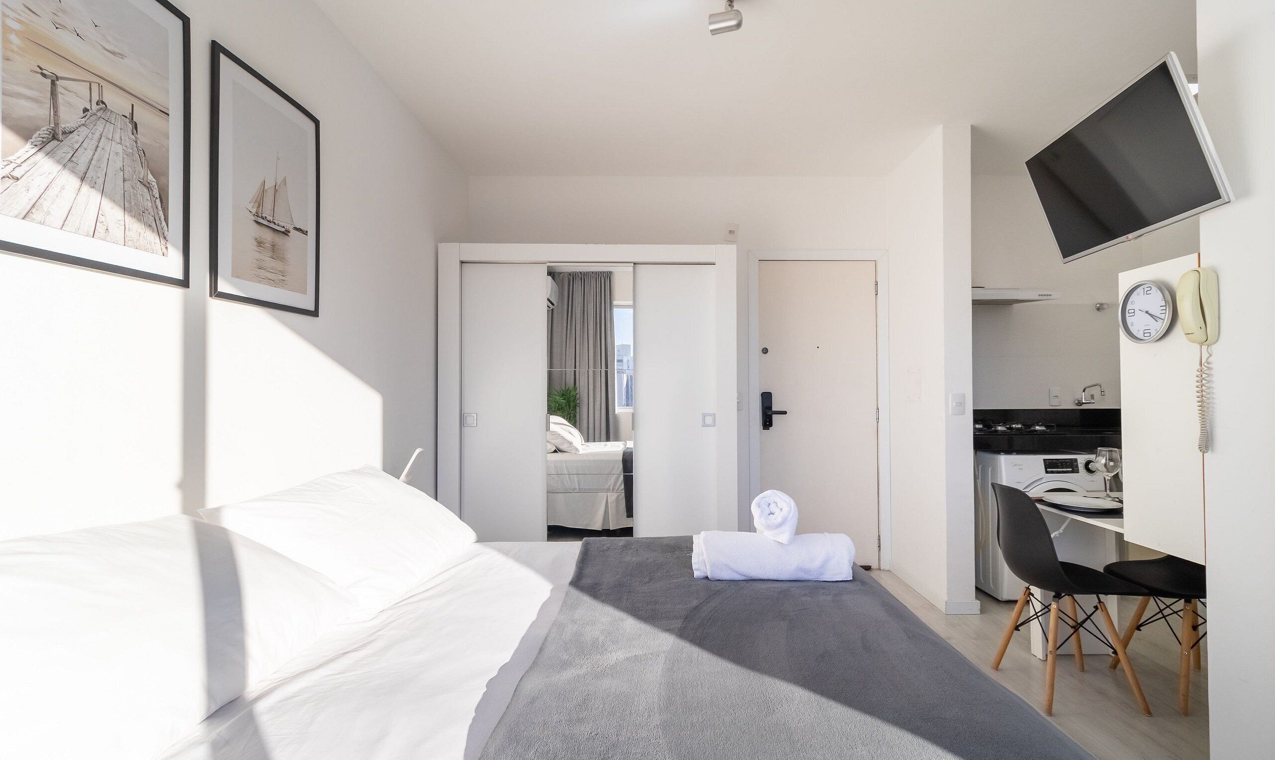 A hotel room with a bed, a desk, a chair, a TV, and a door leading to a balcony.