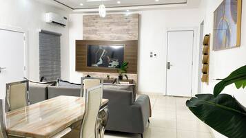 Un salon moderne comprenant un coin repas, un téléviseur à écran plat fixé à un mur en bois et une grande plante.