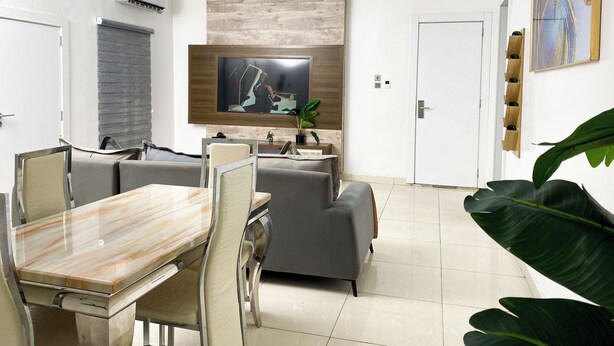 Una sala de estar moderna con comedor, un televisor de pantalla plana montado en una pared de madera y una planta grande.