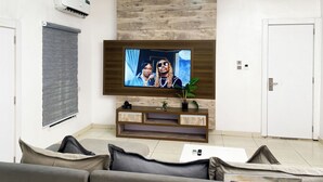 Una sala moderna con una televisión de pantalla plana montada en una pared de madera, un sofá, una mesa de centro y una planta pequeña sobre una consola de madera.