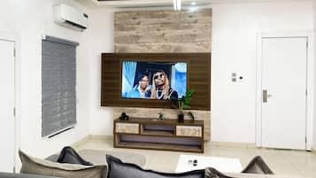 Un salon moderne avec un téléviseur à écran plat fixé à un mur en bois, un canapé, une table basse et une petite plante posée sur une console en bois.