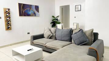 Un salon moderne avec un canapé d’angle gris, une table basse blanche et un meuble à vin en bois.