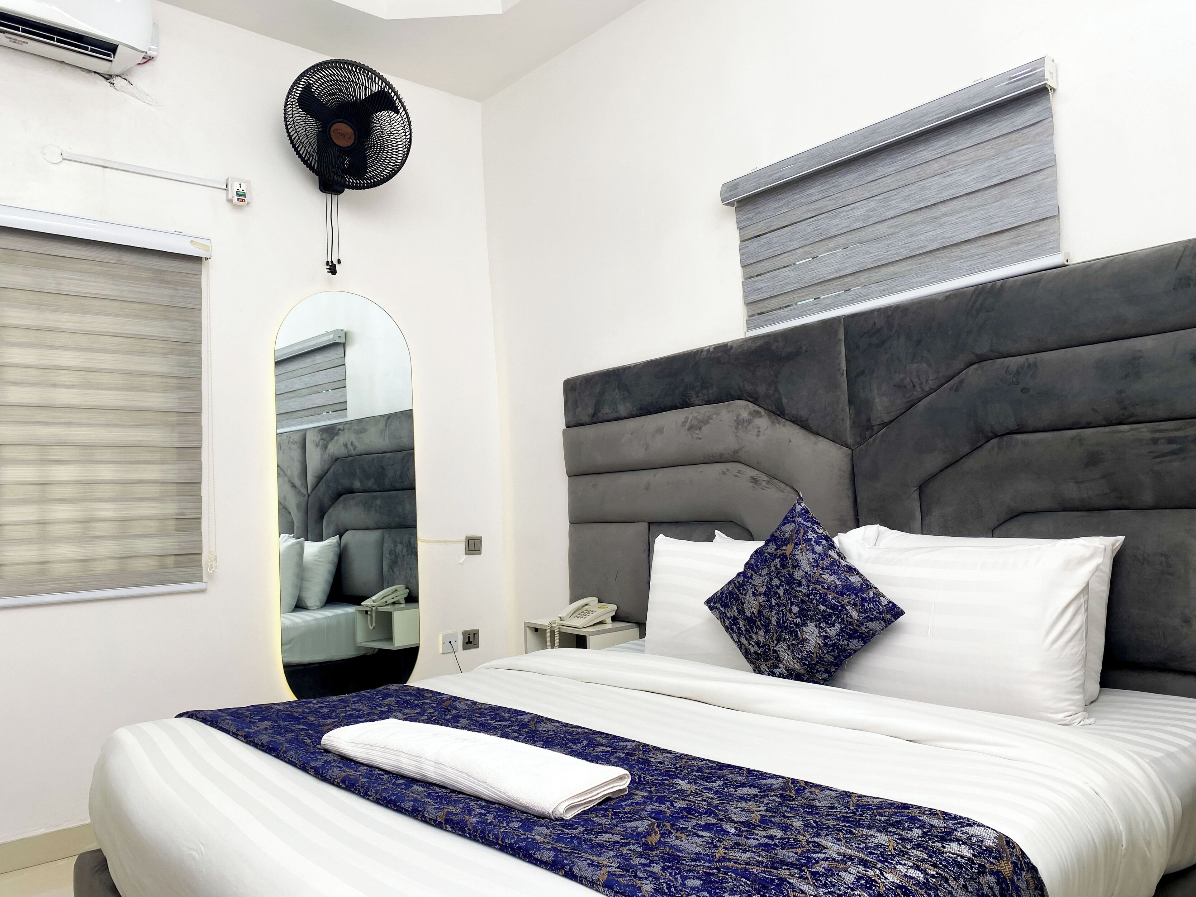 Une chambre d’hôtel moderne avec un grand lit, une table de chevet avec un téléphone, un miroir et une fenêtre avec des stores.