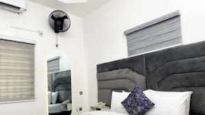 Una habitación de hotel moderna con una cama grande, una mesita de noche con teléfono, un espejo y una ventana con persianas.