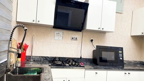 Una cocina con armarios blancos, un microondas negro, una estufa a gas y un lavabo con escurreplatos.