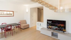 Een moderne woonkamer met een eethoek, een bank, een televisie en een trap.