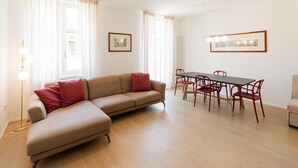Een moderne woonkamer met een beige modulaire bank, een eettafel met rode stoelen en ingelijste foto's aan de wand.