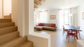 Een moderne woonkamer met een bank, een eettafel en stoelen. Een trap leidt naar een hoger niveau.