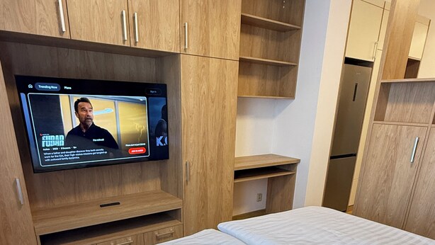 A bedroom with a bed, wooden wardrobe, and a television displaying a movie.