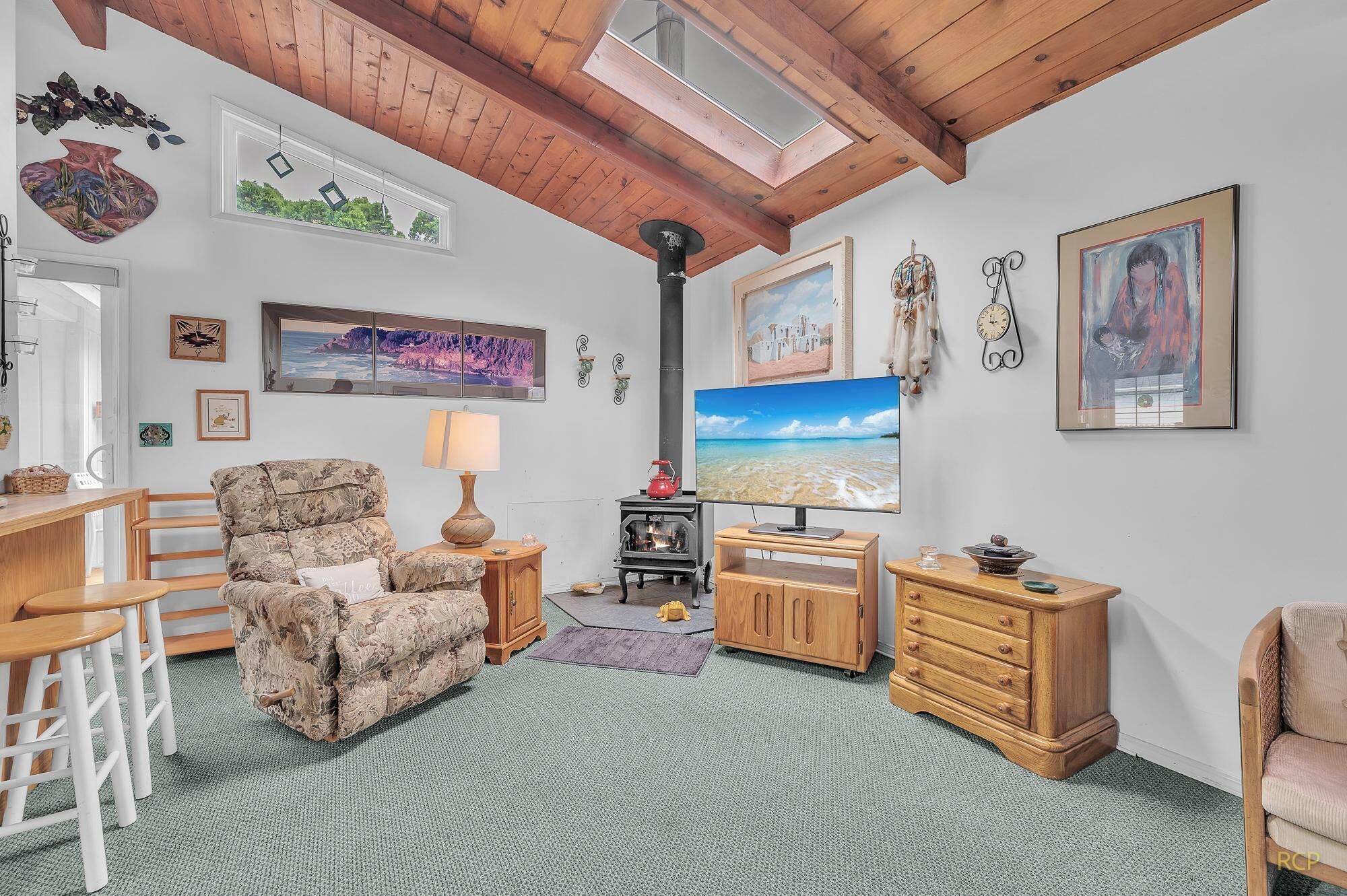 A cozy living room with a wooden ceiling, a fireplace, a television, and various wall decorations.