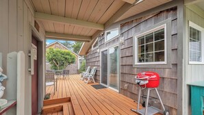 Een houten terras met een barbecue, tuinmeubilair en een schuifdeur naar een overdekte patio.