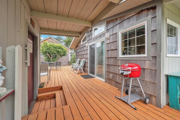 A wooden deck with a barbecue grill, outdoor furniture, and a sliding glass door leading to a covered patio area.