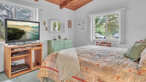 Een slaapkamer met een houten plafond, een bed met bloemenbeddels, een televisie op een houten dressoir en uitzicht op het landschap door een raam.
