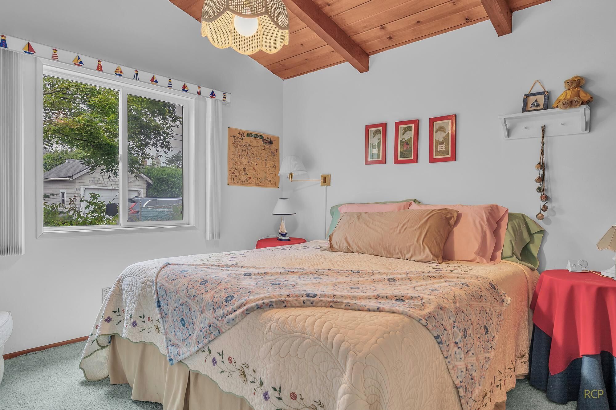 A cozy bedroom with a large bed, a window with a view, a map on the wall, and a small shelf with decorative items.