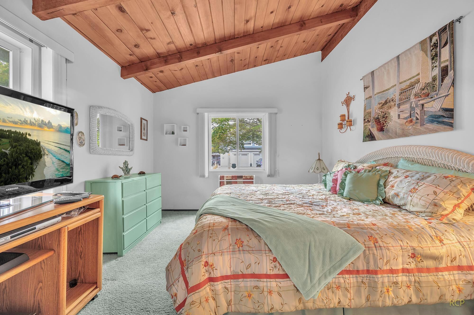 Une chambre à coucher avec un lit, une télévision, une commode, une fenêtre et un tableau.