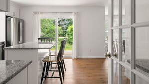 A modern kitchen with a granite countertop, a stainless steel refrigerator, and a dining area with a table and chairs.