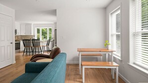 A modern living room with a teal sofa, a wooden coffee table, and a dining area with a kitchen in the background.