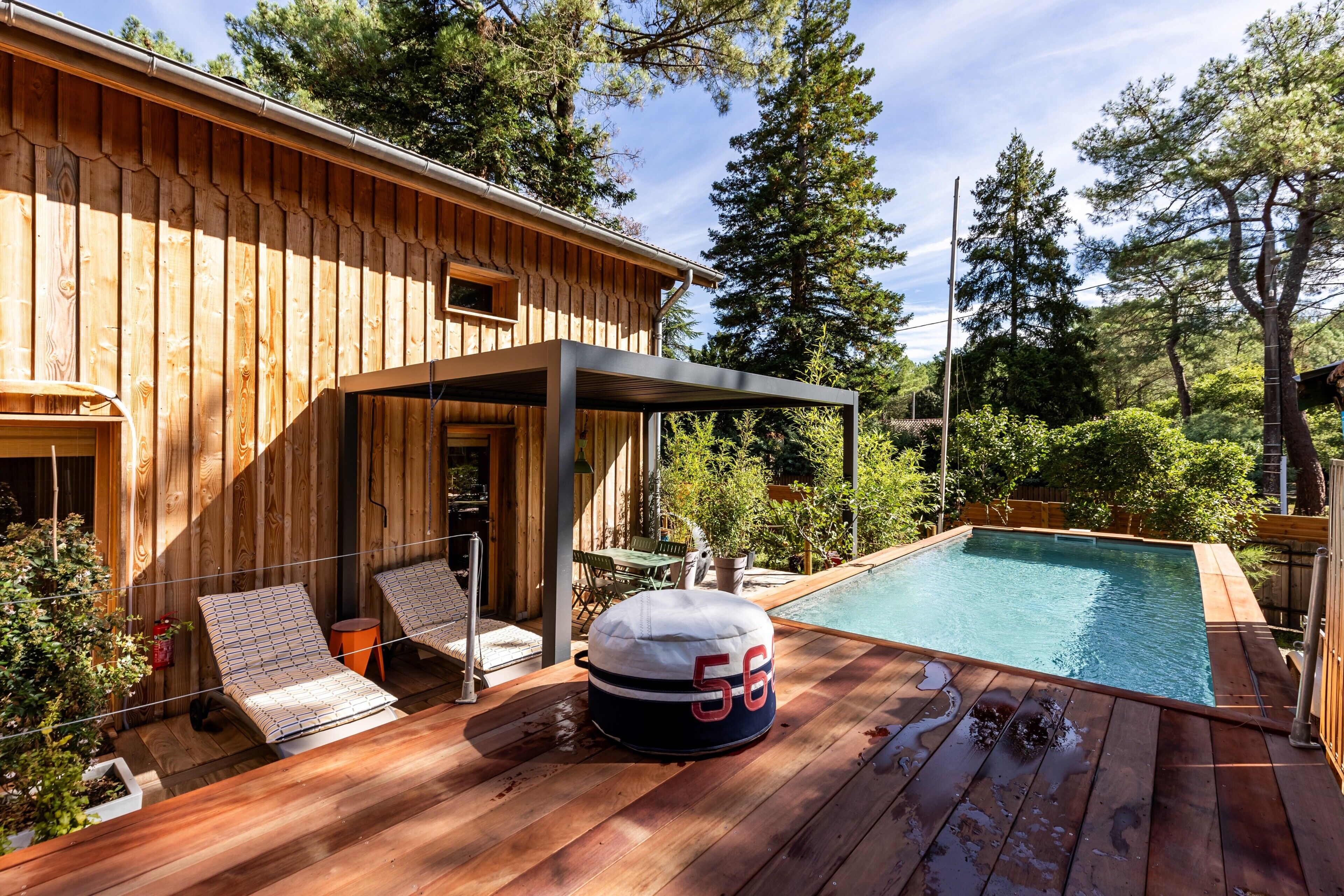 A wooden house with a pool, lounge chairs, and a covered deck area.