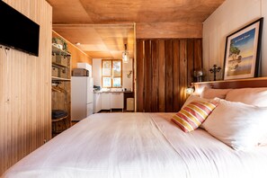 Quarto com cama, escrivaninha e cozinha compacta.