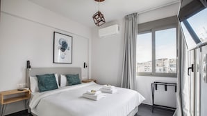 Una camera d'albergo moderna con un letto grande, un comodino, un quadro incorniciato, un condizionatore d'aria e una finestra con tende.