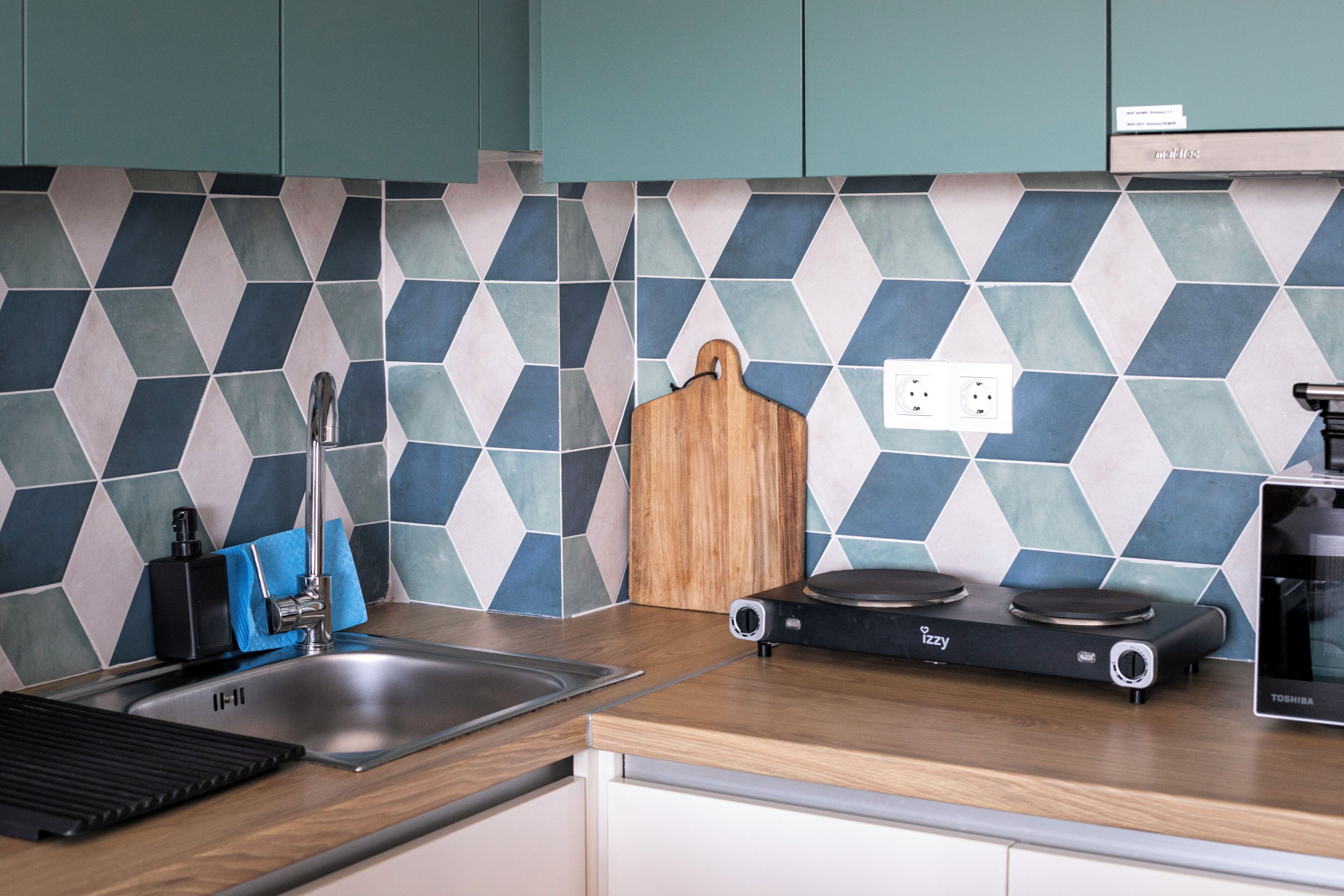 A kitchen with a modern design, featuring a sink, a cutting board, and a portable electric stove.