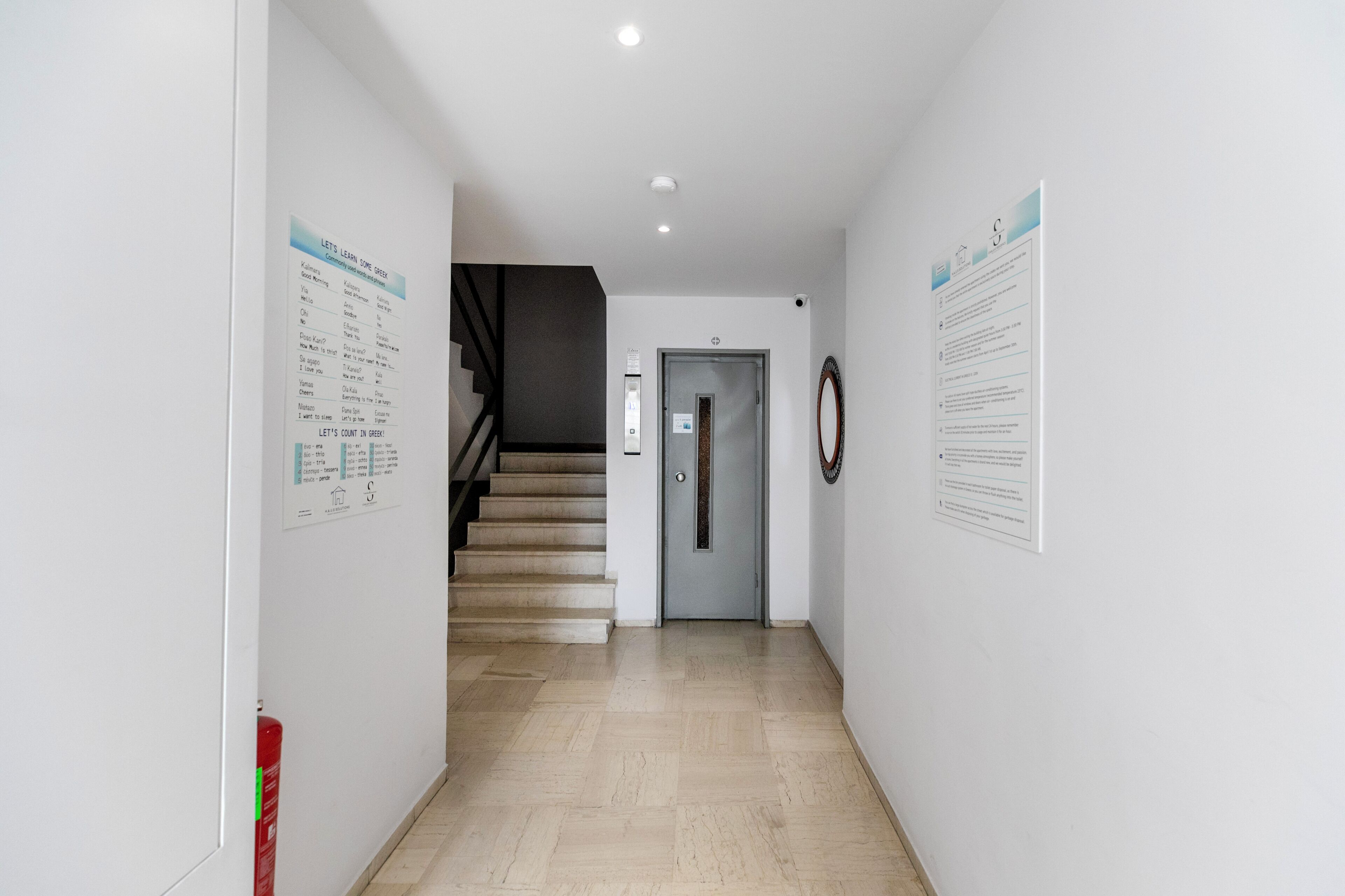 A hallway with a staircase leading to a door, white walls, and informational posters.
