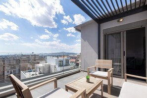 Un balcón con vista a la ciudad, mobiliario de madera y una puerta corredera de vidrio.