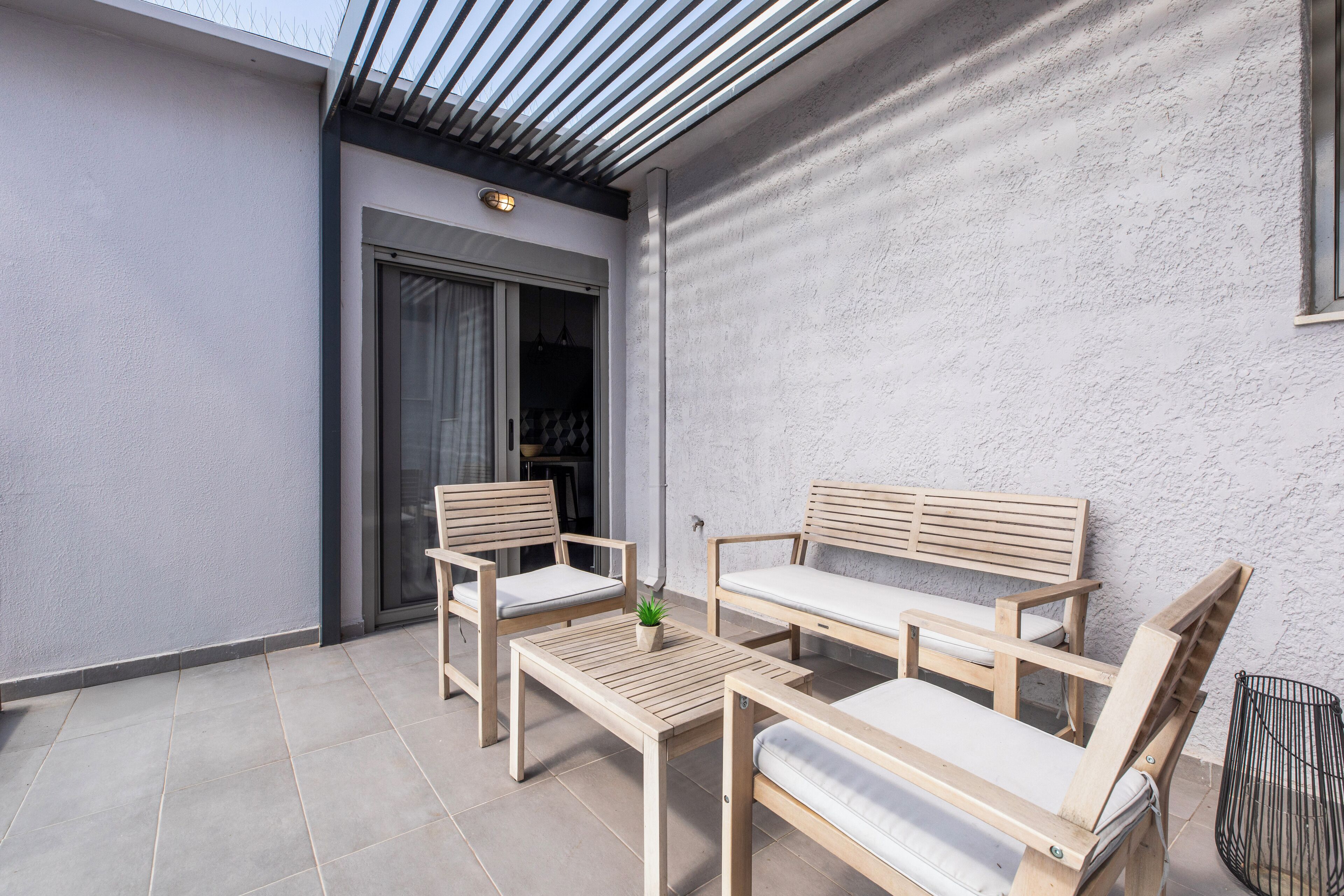 Un patio con muebles de madera, incluyendo una mesa y sillas, y una pequeña planta en maceta.
