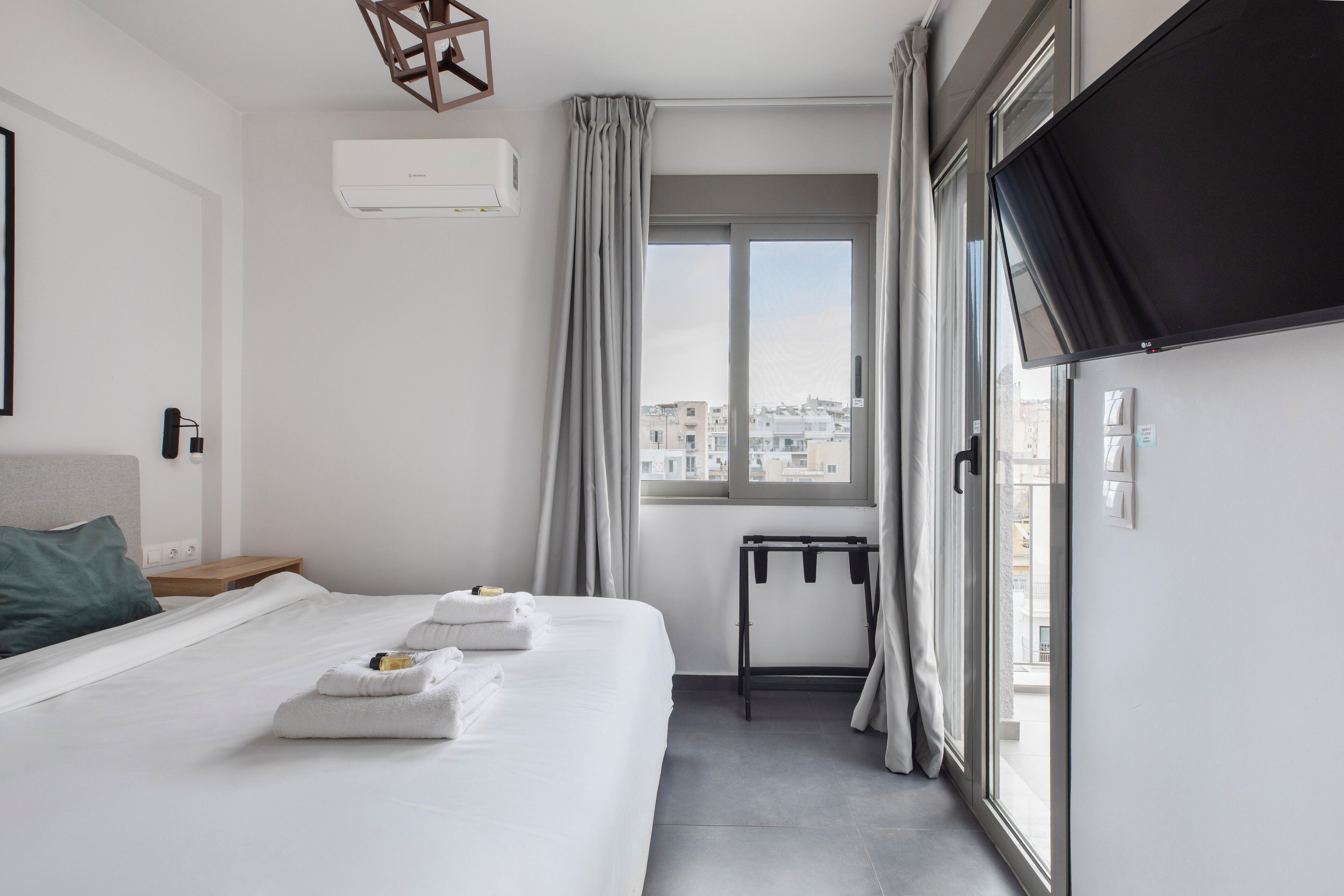A modern hotel room with a large bed, a TV, and a view of the city through the window.