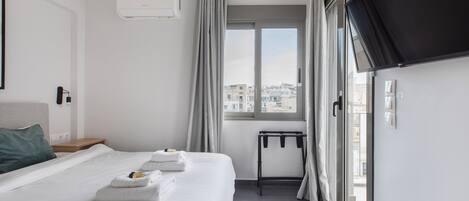 A modern hotel room with a large bed, a TV, and a view of the city through the window.