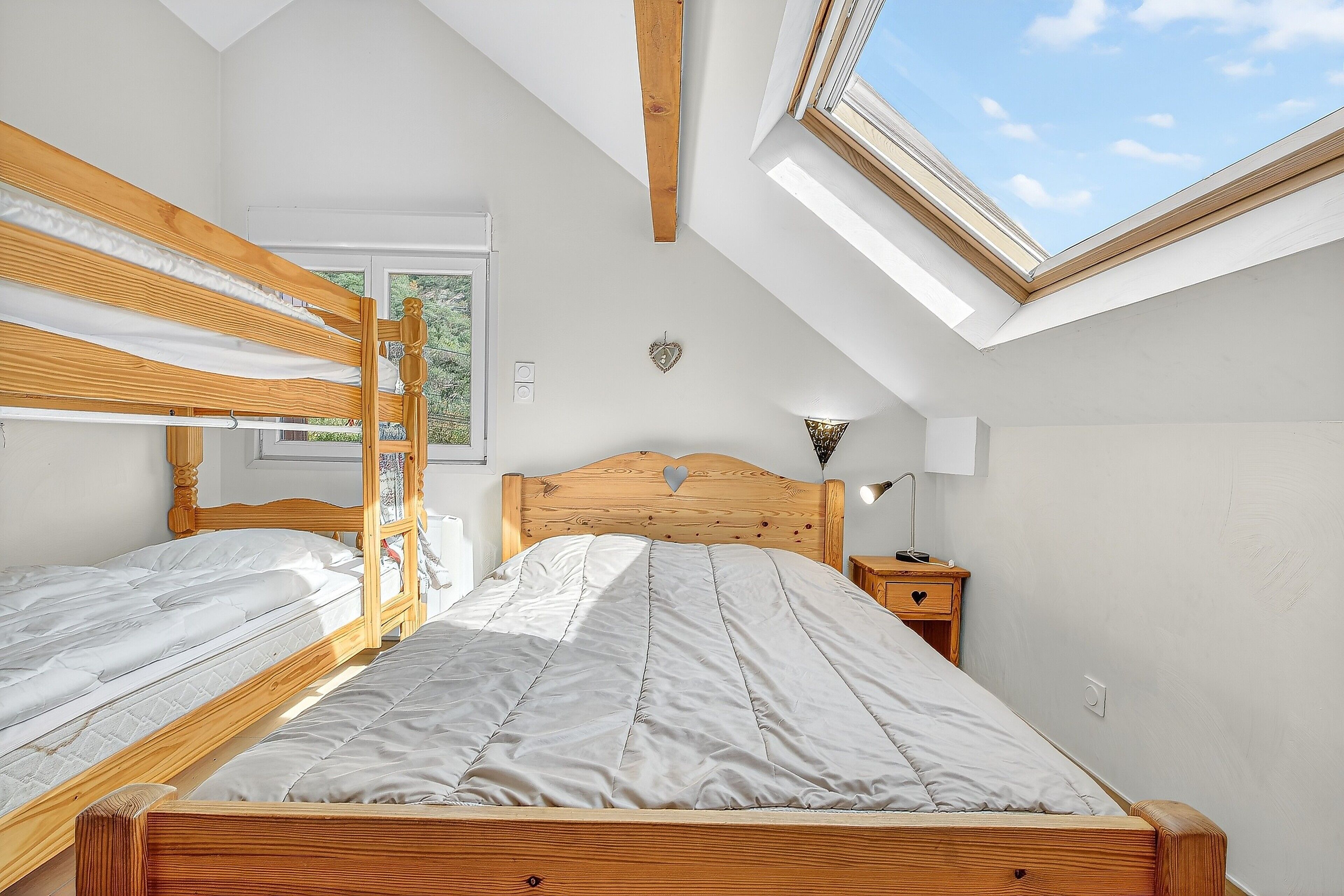 Une chambre avec un plafond en pente, un lit en bois, une table de chevet et une fenêtre.
