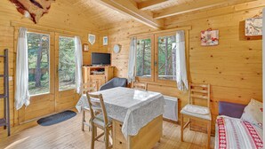 Ein Holzblockhaus-Interieur mit Esstisch, Stühlen, Fernseher und einem Bett.