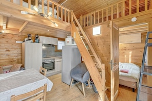 A wooden cabin interior with a kitchen, dining area, and a loft bedroom. - Chalet 'Les Chalets' with Mountain View, Shared Terrace and Private Garden (Méolans-Revel)