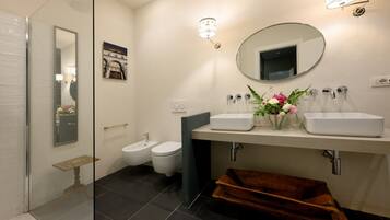 Une salle de bain moderne avec une douche à parois de verre, un bidet, un lavabo blanc avec un miroir et un vase de fleurs.