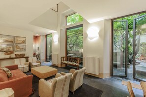 A spacious living area with a large sofa, armchairs, and a coffee table. There are framed artworks on the wall, a fireplace, and a view through large glass doors to an outdoor area. - Duomo Luxury Apartment with plunge pool (Firenze)