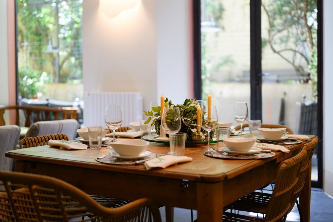 Une table à manger dressée avec des assiettes, des verres et des bougies, donnant sur un paysage verdoyant.
