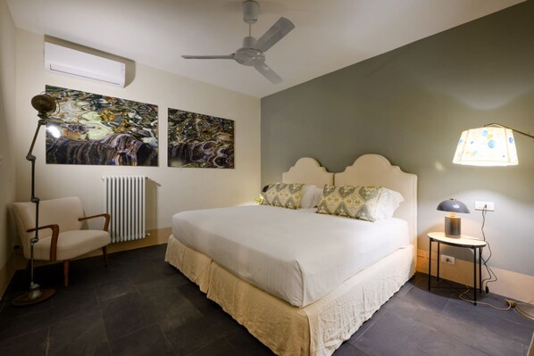 A bedroom with a bed, a chair, a floor lamp, and two paintings on the wall.