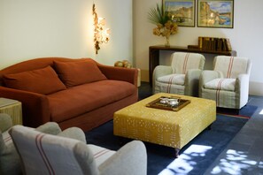A living room with a brown sofa, two armchairs, a coffee table, and a side table. There are framed pictures on the wall and a small plant on the side table.
